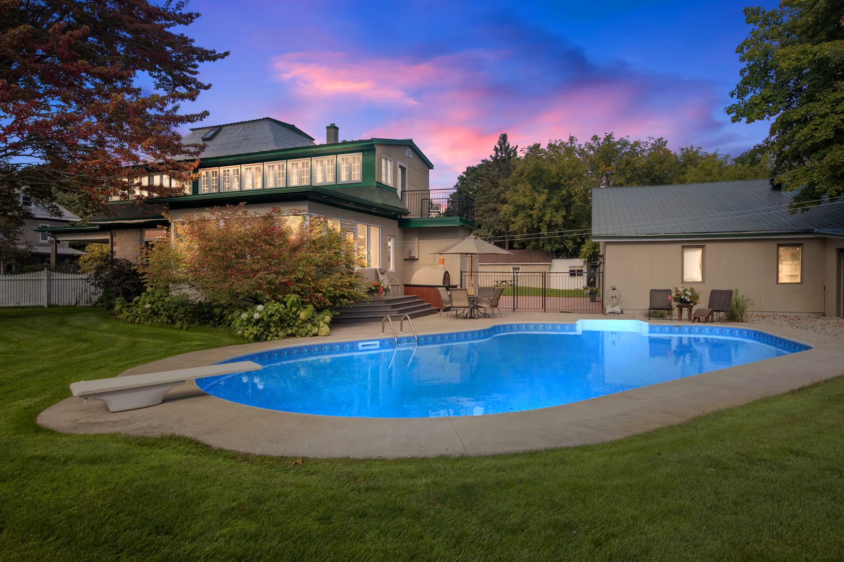 A large home and its pool at dusk under a pink sky